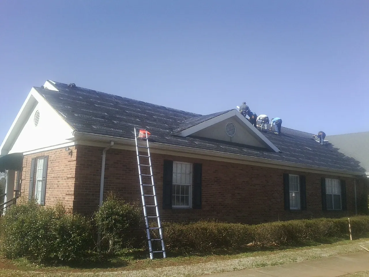 Crew tearing shingles off a brick ranch roof with a ladder set — Emergency Roof Repair work by our crew in Afton