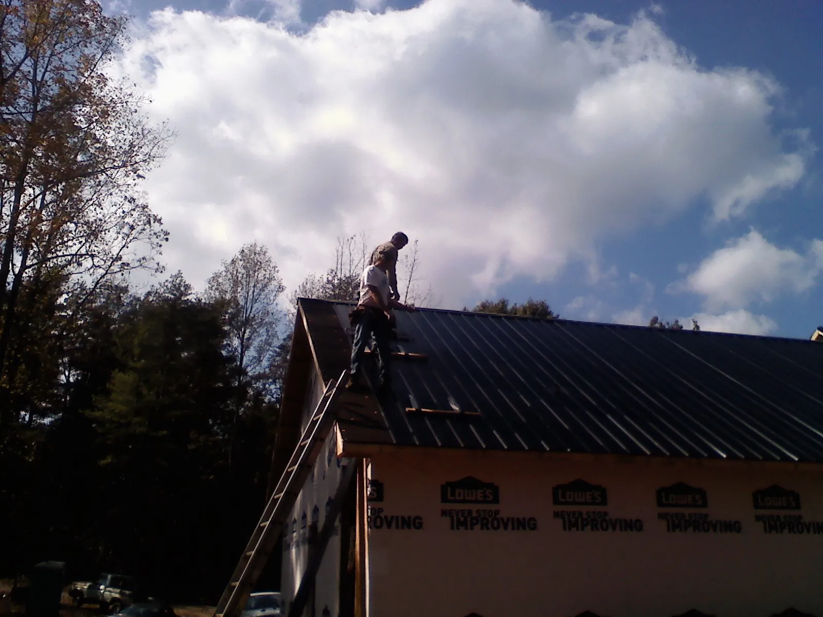 Roofer fastening dark metal panels high against a cloudy sky, from a Roof Inspection job in Afton